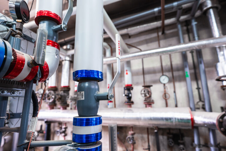 Instalacja wodno-kanalizacyjna w oczyszczalni ścieków w Bytomiu: metalowe rurociągi i zawory, elementy czerwone i niebieskie, rozwiązania Kelvin.