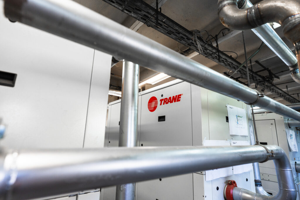 Wnętrze instalacji w oczyszczalni: stalowe rury, przewody i moduł z logo TRANE, w systemie sterowania i AKPiA