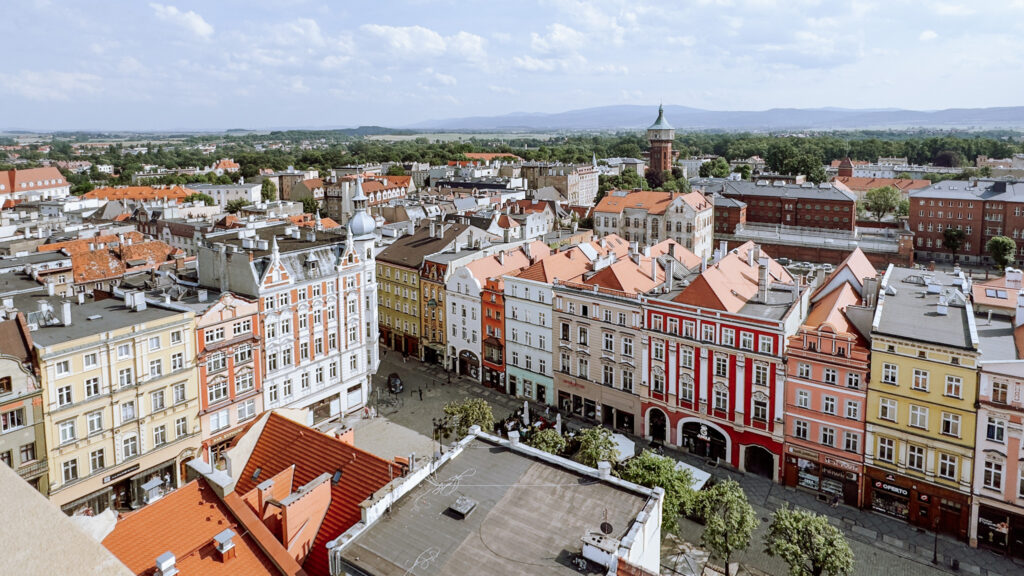 Z Wieży Ratuszowej w Świdnicy widać rynek, zabytkowe kamienice i rozległą panoramę miasta z wieżą w tle.